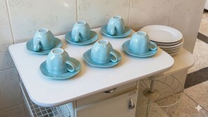 Una encimera de cocina con seis tazas y platillos azules, una pila de platos blancos y un salpicadero de azulejos blancos.