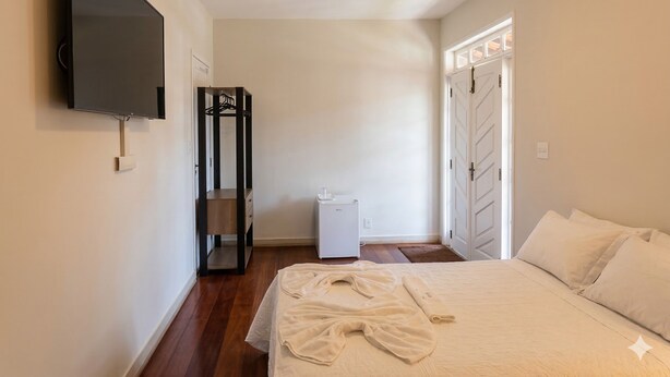 Un dormitorio con cama, televisor, armario, calefactor y puerta.