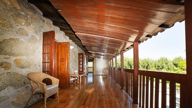 Portico in legno coperto con pareti in pietra, mobili in legno e vista sul verde.