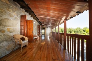 A covered wooden porch with stone walls, wooden furniture, and a view of greenery. - Casa da Eira by Quantique (Prozelo)