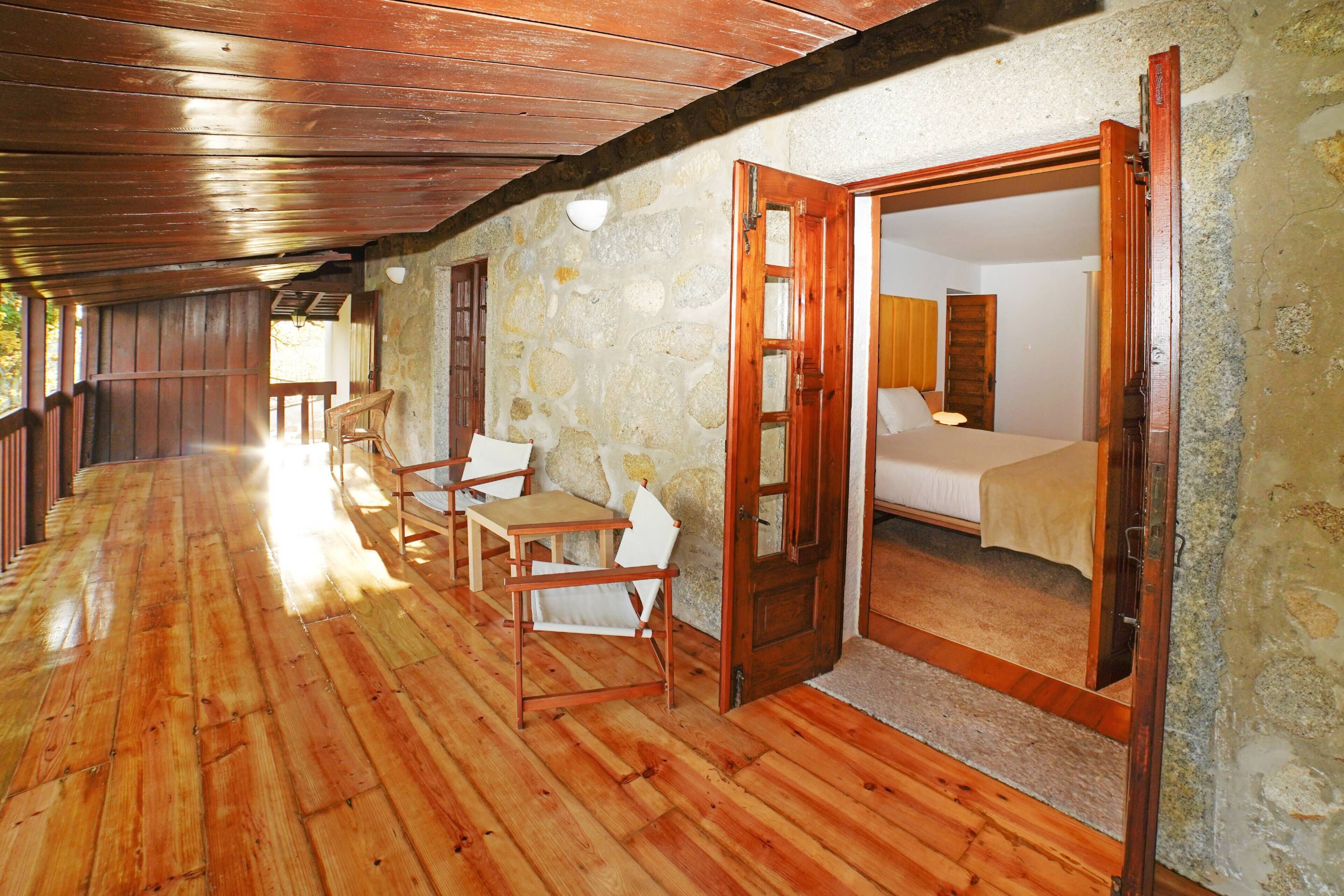 A wooden-floored corridor leading to a bedroom with a bed, a chair, and a table.