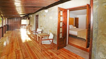 A wooden-floored corridor leading to a bedroom with a bed, a chair, and a table.