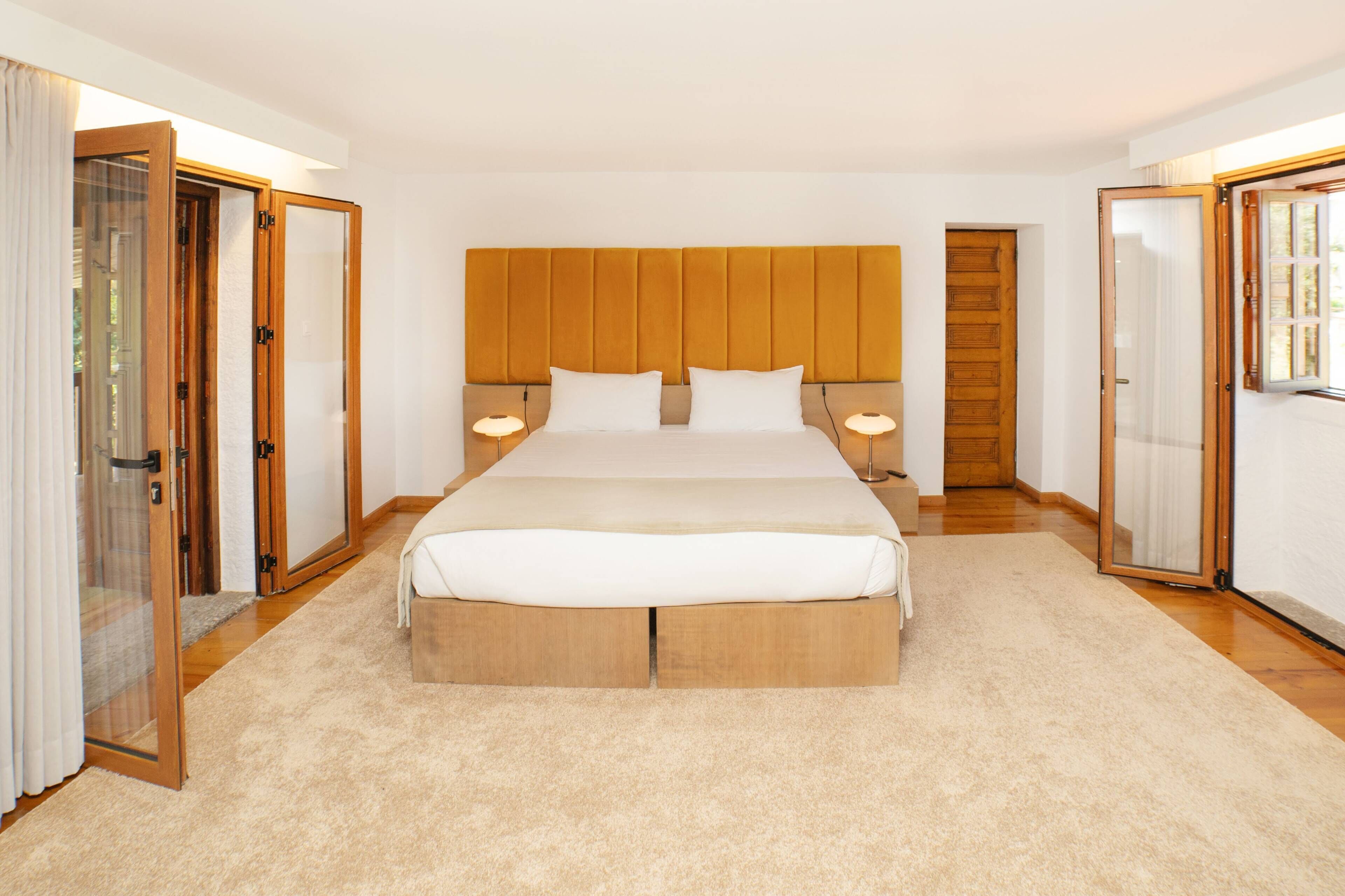 Quarto com cama grande, cabeceira de madeira, abajures e piso coberto por carpete.
