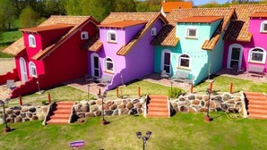 Una fila di case colorate con tetti rossi, viola e color acquamarina, scalini in pietra e un prato.