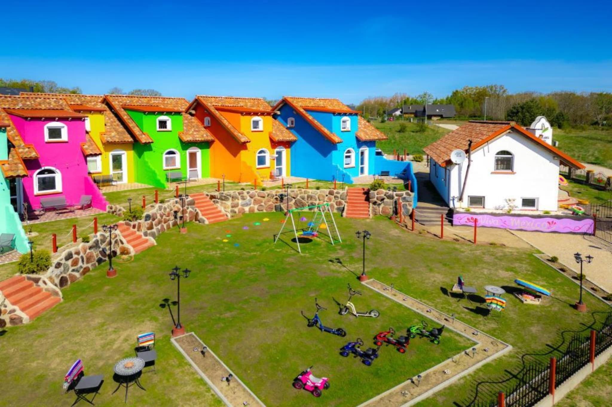 Colorful houses with a grassy yard, a swing set, and a small pond.