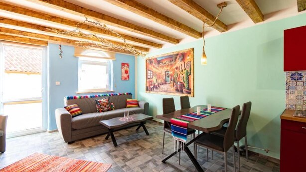 Un salon chaleureux avec un canapé, une table basse et une table à manger avec des chaises. Une fenêtre laisse entrer la lumière naturelle et un tableau coloré orne le mur.