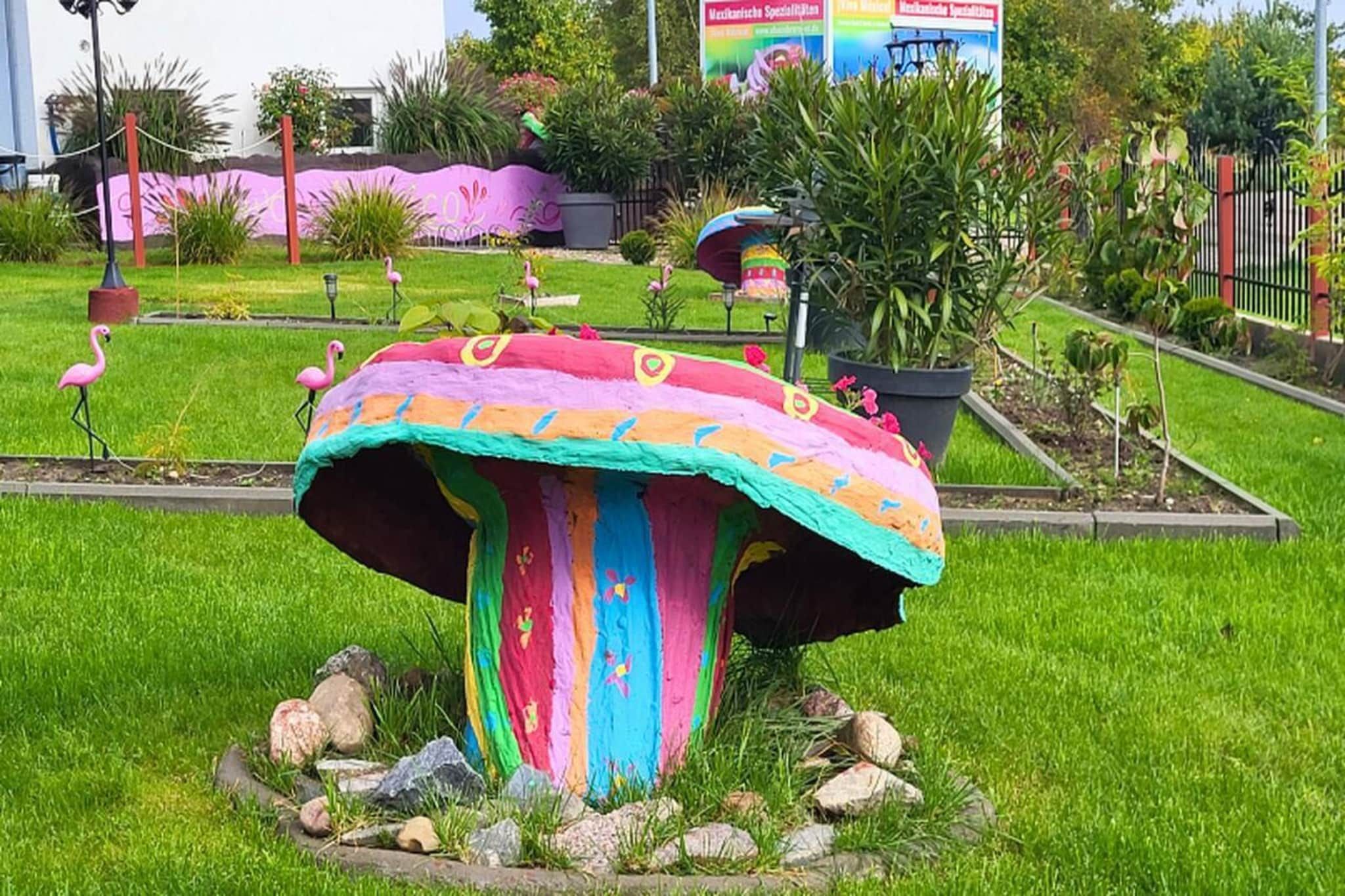 A colorful mushroom-shaped structure in a garden with flamingos nearby.