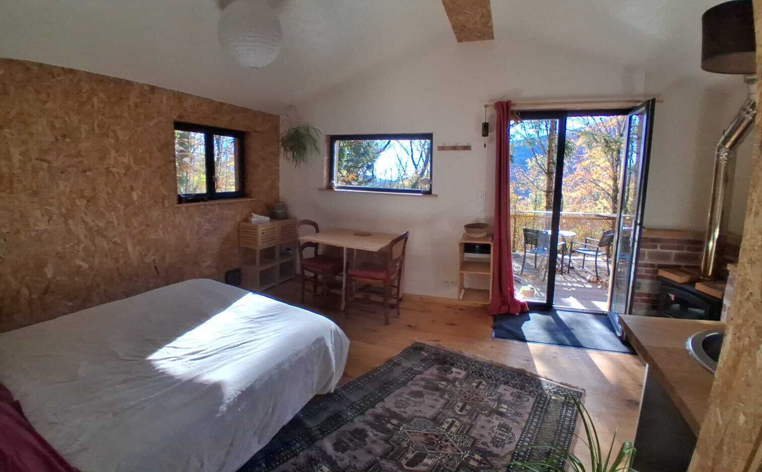 Ein Schlafzimmer mit Bett, Schreibtisch, Stuhl, Teppich und einer Schiebetür, die zu einem Außenbereich führt.