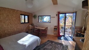 A bedroom with a bed, a desk, a chair, a rug, and a sliding glass door leading to an outdoor area. - Isolated cabin in the forest (Lespinassière)