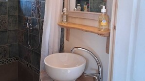 A bathroom with a shower, a sink, a mirror, and a shelf with toiletries. - Isolated cabin in the forest (Lespinassière)