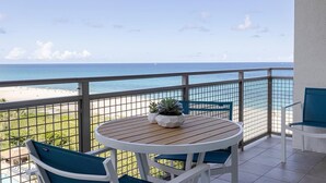 Een balkon met uitzicht op het strand, een ronde tafel met stoelen en een plant in pot.
