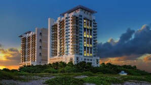 Een hoog hotel met meerdere balkons, een plat dak en uitzicht op het strand bij zonsondergang.