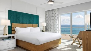 Een hotelkamer met een groot bed, twee nachtkastjes, een bureau en uitzicht op de oceaan.