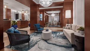 Een moderne hotellobby met een receptiebalie, zithoek en een kroonluchter.