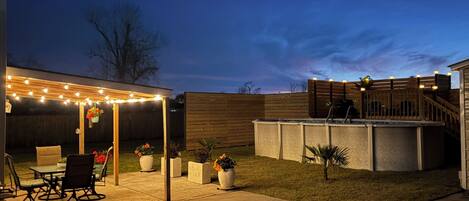 A backyard patio with a covered seating area, a fire pit, and a wooden deck.