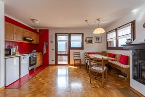 A kitchen with red walls, a dining area with a wooden table and chairs, and a fireplace. - Wonder Condominium (Selva di Cadore)