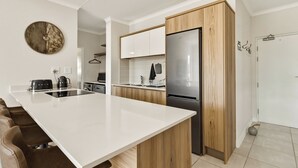 Une cuisine moderne dotée d’un grand îlot central, de meubles en bois, d’un réfrigérateur en acier inoxydable et d’une horloge murale.