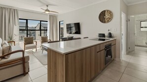 Une cuisine moderne dotée d’un îlot central, d’un coin repas avec des chaises, d’un téléviseur à écran plat et d’une grande fenêtre agrémentée de rideaux.