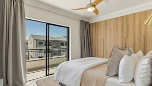 Une chambre à coucher avec un lit, des rideaux, un ventilateur de plafond et une vue sur l’extérieur, accessible par une porte coulissante.