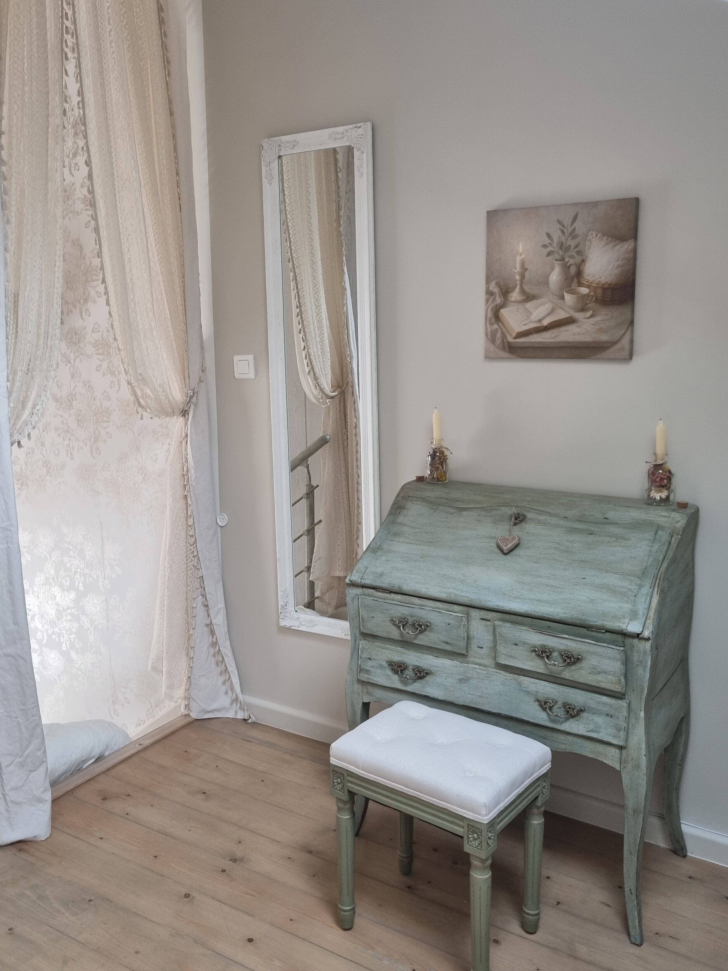 Een kamer met een houten vloer, een groene dressoir met laden, een spiegel en een schilderij aan de muur.