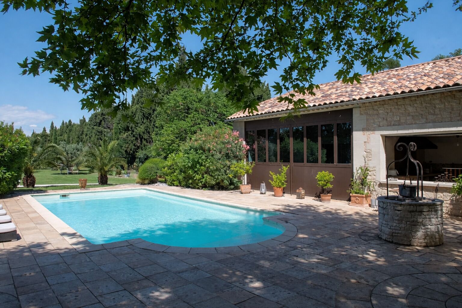 A swimming pool with a stone deck, a stone fountain, and a building with a tiled roof and windows.