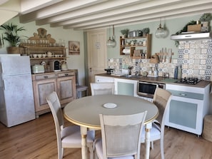 A kitchen with wooden cabinets, a dining table with chairs, a refrigerator, a stove, and various kitchen utensils. - Mas des Trois V - View Vignes & Ventoux - Gîte de Charme Premium 2 to 4 Adults (Sarrians)