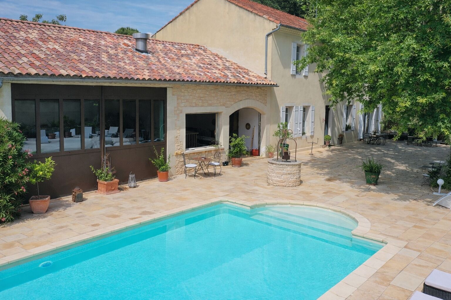 A swimming pool with a stone deck, a covered patio area, and a building with a tiled roof.