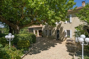A courtyard with a large tree, a building with a tiled roof, and outdoor seating. - Mas des Trois V - View Vignes & Ventoux - Gîte de Charme Premium 2 to 4 Adults (Sarrians)
