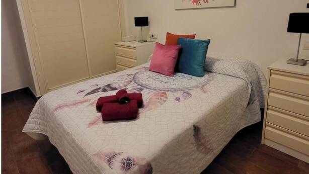A bedroom with a bed, pillows, a nightstand, a lamp, a wardrobe, and a wall art piece. - Apartment With Large Terrace in Almeria (Vera)