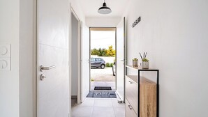 A hallway with a door leading to a car parked outside, a small potted plant on a shelf, and a black pendant light. - A relaxing break in the countryside, 5 minutes from the sea (Martigues)