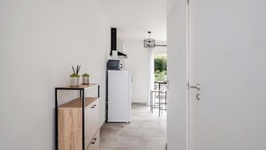 A narrow hallway with a white refrigerator, a small table with chairs, and a potted plant on a shelf. - A relaxing break in the countryside, 5 minutes from the sea (Martigues)