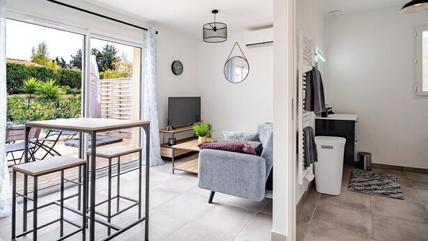 A modern living room with a TV, seating area, and a view of the garden. - A relaxing break in the countryside, 5 minutes from the sea (Martigues)