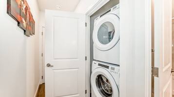 A laundry room with two stacked washing machines, a white door, and a hallway.