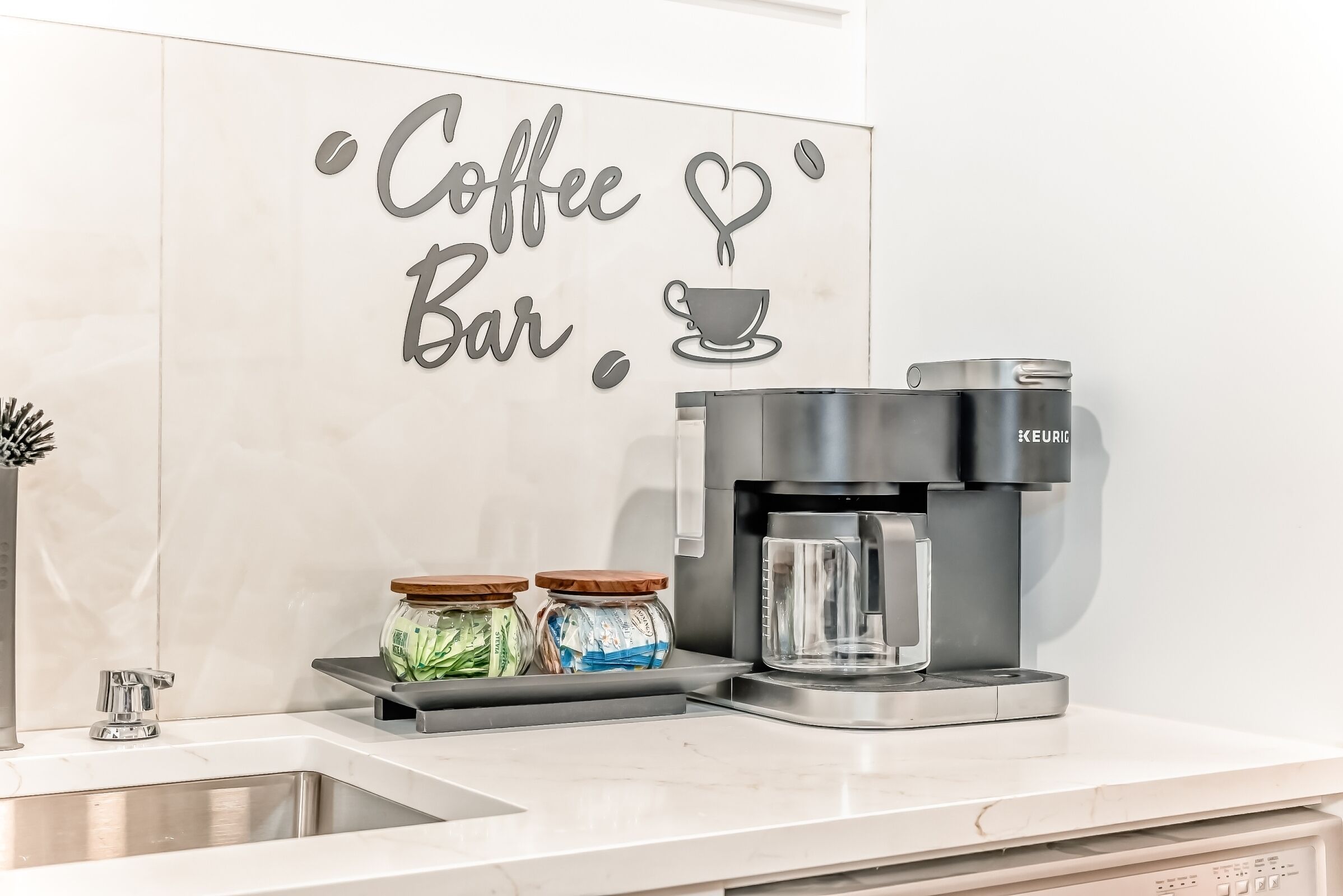 A kitchen area with a coffee machine, two jars of condiments, and a sign that reads 'Coffee Bar'.