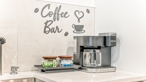 Uma área de cozinha com uma cafeteira, dois potes de temperos e uma placa com a inscrição 'Coffee Bar'.
