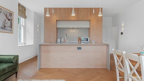 Eine moderne Küche mit Holzschränken, Pendelleuchten, einer eingebauten Mikrowelle und einem Essbereich mit einem grünen Sofa und weißen Stühlen.