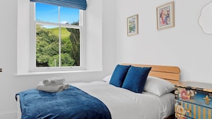 Ein Schlafzimmer mit Bett, einem Fenster mit Aussicht, einem Schminktisch und zwei gerahmten Bildern an der Wand.