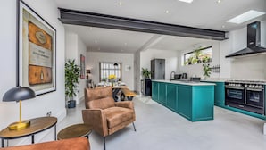 Eine moderne Küche mit einer zentralen Kochinsel, ein Essbereich mit Tisch und Stühlen sowie ein Wohnzimmer mit Sofa und Lampe.