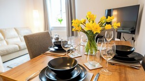 Une table à manger dressée avec des assiettes noires, des verres transparents et un vase rempli de fleurs jaunes.