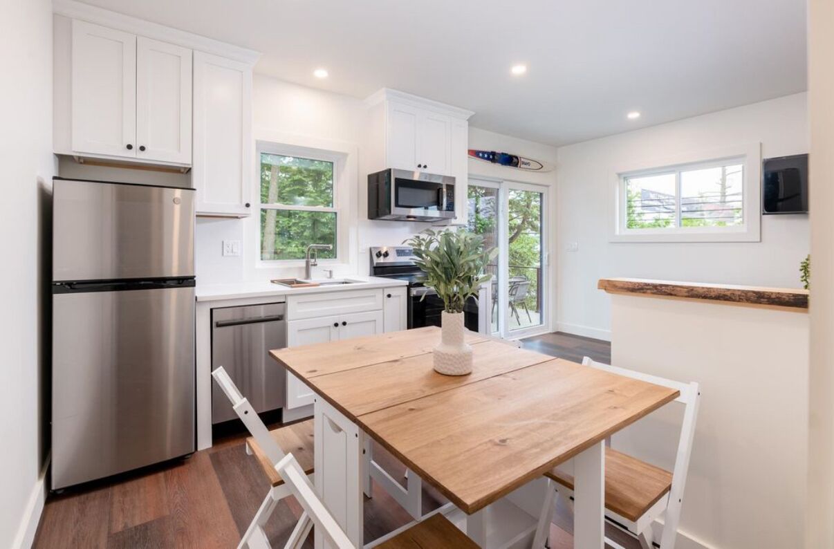 Une cuisine moderne avec des meubles blancs, des appareils en acier inoxydable et une table à manger en bois.