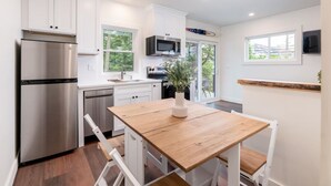 A modern kitchen with white cabinets, stainless steel appliances, and a wooden dining table. - Lakeside Cottage Retreat – 4 Loft Style Cottages with Dock Slip - Weirs Beach (Laconia)