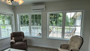 Una habitación con ventanas amplias, ventilador de techo, una silla, una mesa y un equipo de aire acondicionado.