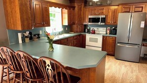 Una cocina con armarios de madera, una isla central con sillas, un refrigerador y un microondas.