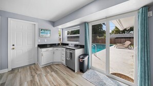 Una cocina con isla integrada, puerta corrediza de vidrio a un patio trasero con piscina, y una puerta que da a otra habitación.