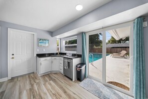 A kitchen with a built-in island, a sliding glass door to a backyard with a pool, and a door leading to another room. - Naples Pool Retreat l Mini Putt + Private Yard (Naples)