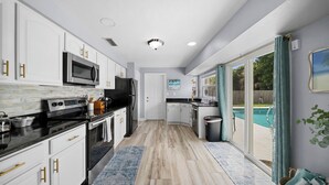 Una cocina moderna con armarios blancos, electrodomésticos de acero inoxidable y un amplio ventanal con vistas a una piscina.