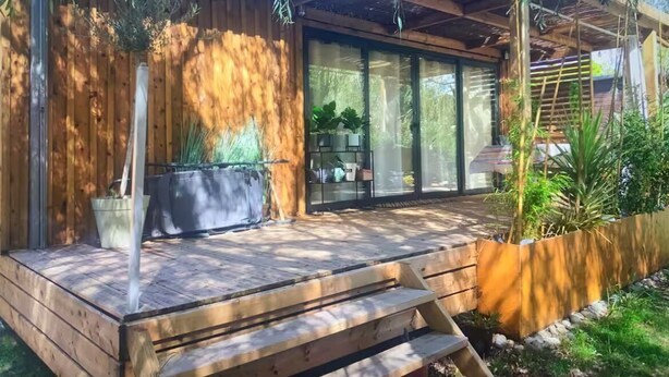 Ein modernes Haus mit Holzterrasse, großen Fenstern und Topfpflanzen.