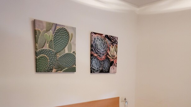 A bedroom with a wooden headboard, a patterned bedspread, two pillows, a bedside table with a lamp, and two wall-mounted artworks. - Charming Apartment With Garden in Almeria (Vera)