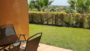 A patio with a table and chairs, a well-maintained lawn, and a view of palm trees and distant landscape. - Charming Apartment With Garden in Almeria (Vera)