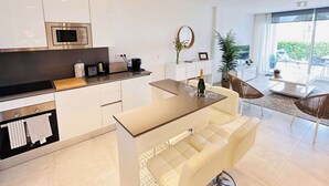 A modern kitchen with a microwave, toaster, and coffee maker. There is a dining area with a table and chairs, and a large window offering a view of the outdoors. - Casa Banderas - 2 BR (6p) - Pool view & mountains - La Cala De Mijas (Cala de Mijas)